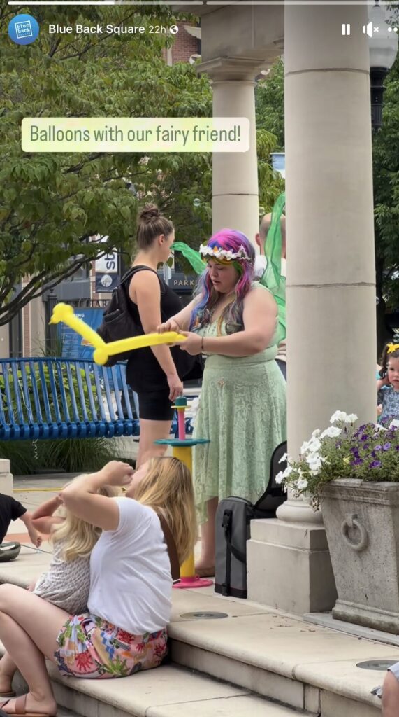 A screen shot from the instagram story of Blue Back Square in CT that says "balloons with our fairy friend" and shows Alexis twisting balloons at an outdoor party